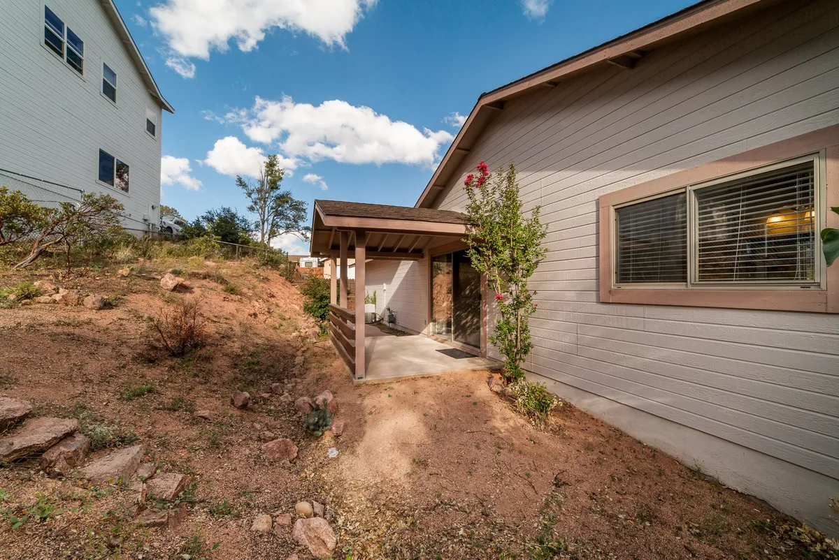 This exterior image presents a covered porch overlooking a landscaped path with decorative plants, and a glimpse of neighboring houses. The scene evokes a sense of community while retaining privacy, with the porch acting as a spot to enjoy the outdoors and peaceful surroundings.
