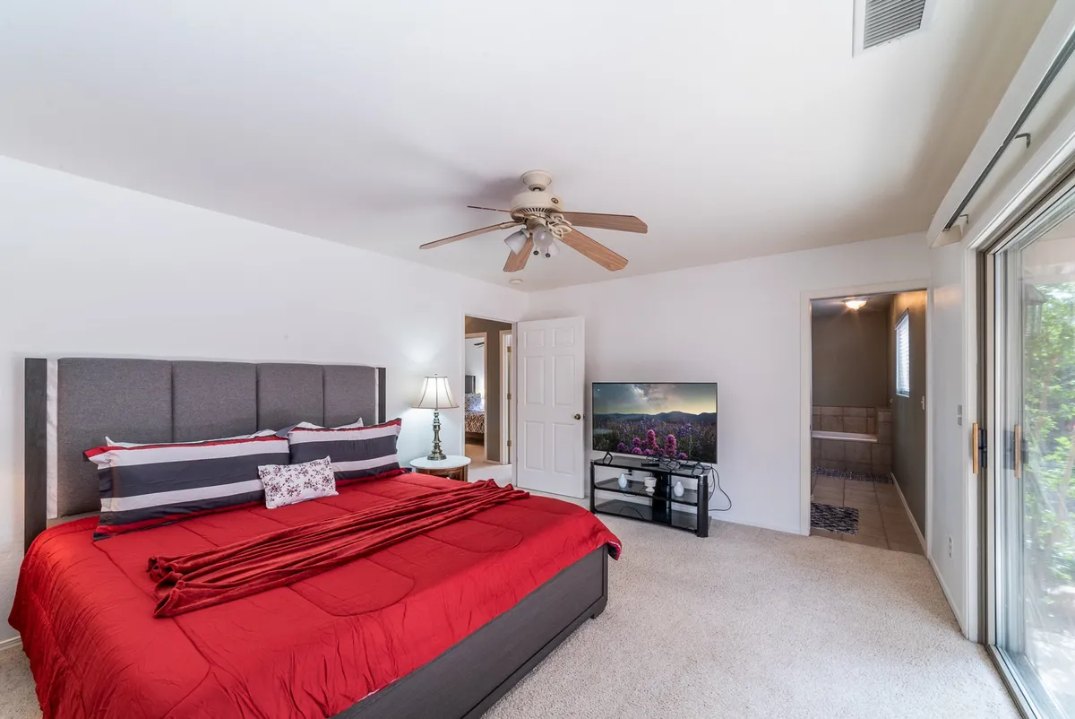 A spacious bedroom featuring a large red bed as the focal point, with a television and a lamp on the nightstand. The room exudes an inviting atmosphere, ideal for relaxing or watching TV from the comfort of bed.