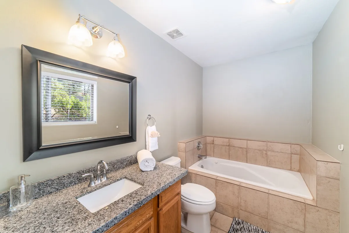 A serene bathroom with a granite countertop, framed mirror, and inviting bathtub. The room feels fresh and soothing, ideal for a rejuvenating bath or self-care routine.