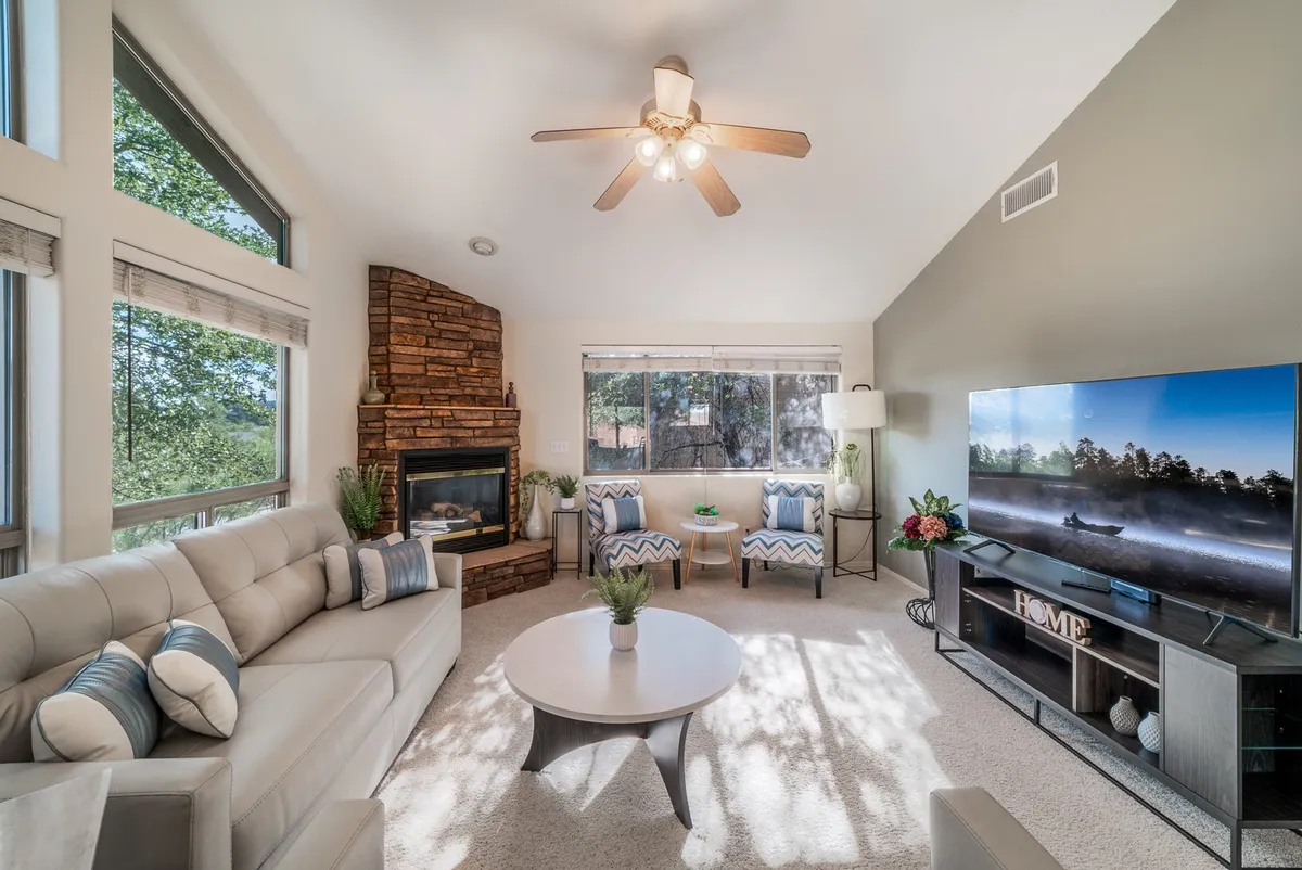A spacious great room featuring plush sofas and armchairs arranged around a coffee table, with a cozy gas fireplace and a large-screen TV as focal points. The room is bathed in natural light, creating an inviting space for relaxation and socializing.
