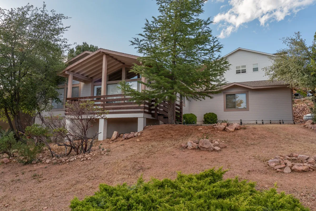 This exterior image features the porch area of the home, surrounded by mature trees and a gently sloped yard. The porch offers a comfortable space for relaxation and connects the house to the outdoors, while the yard hints at opportunities for outdoor activities and gatherings.