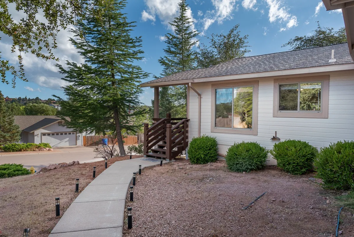 An exterior shot capturing the home's front steps, large windows, a landscaped pathway, and the surrounding trees. The scene is welcoming and suggests easy access to both the house and nearby outdoor amenities.