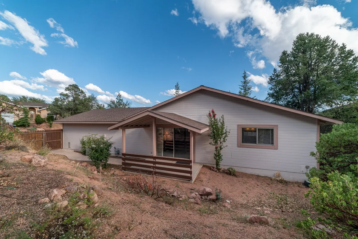 This image showcases the front porch, landscaped yard, and a backdrop of tall trees, creating a sense of privacy and space for outdoor gatherings or quiet moments. The porch is designed for relaxation, with views of the lush surroundings.