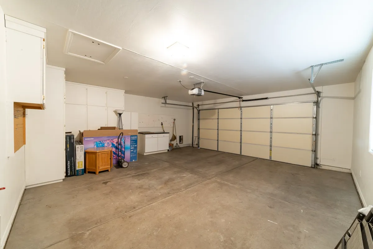 The image displays an interior garage space with a visible garage door, storage cabinets, and a workbench. The space is clean, functional, and ready for both parking and storage needs.