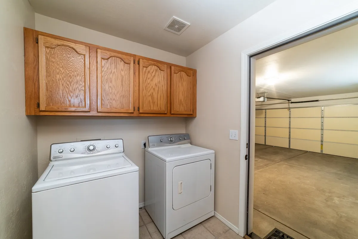 This image shows a well-organized laundry room featuring a washing machine, dryer, and wooden cabinets above for storage. The space is tidy and practical, reinforcing the sense of ease and readiness for doing laundry and managing household essentials.